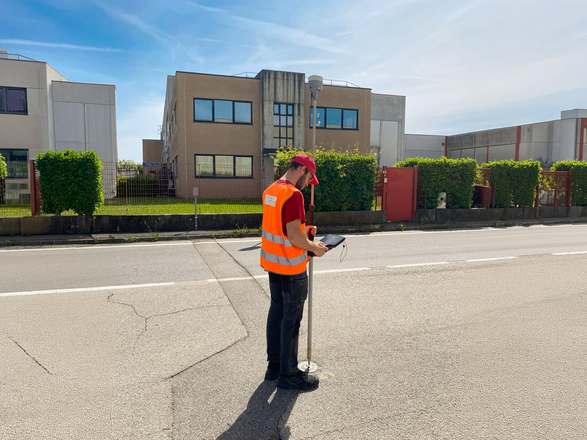 Tecnico Adastra durante un rilievo topografico GNSS con palina GPS e controller in contesto urbano